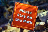 An orange sign that says Please Stay on the Path.