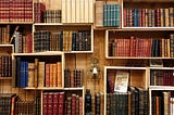 Shelves that look like boxes hold vintage books upon a wooden wall.