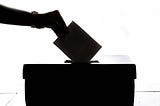 A silhouette of a hand placing a piece of paper in a ballot box.