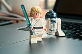 Luke Skywalker with a blue sabre and R2D2 Lego standing on a laptop.