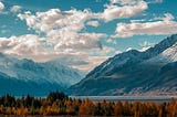 pic of a beautiful landscape- with mountains in the distance — a lake in the middle of the pic — and a forest in the foregrond