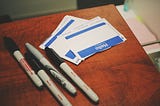 Some name badges on a table with pens. They are blank but ready to be filled in.