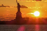 The Statue of Liberty against an orange sunset.