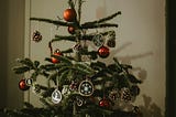 A spindly, sparse real Christmas tree with red bulb ornaments and gold snowflake ornaments.