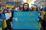 A woman at a protest holding a sign that says, “Pressure Russian Oligarchs”
