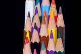 A clump of colorful pencils grouped in alternating heights, with a black background