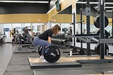 A woman in workout wear grasps a barbell loaded with heavy weights, preparing for a deadlift