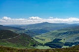 A mountain range in Ireland under a blue sky showing a small road