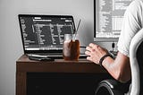 a software engineer sitting on his disk and work with 2 screens and a cold dark drink