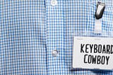 imagem de um crachá escrito Keyboard Cowboy, preso em uma blusa social xadrez azul