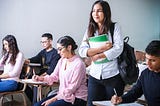 A student stands in a classroom while her classmates study.