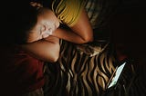 A girl lying on bed and staring at the screen placed near her mindlessly.