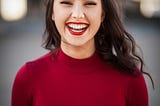 A young brunette lady wearing a red top and red lipstick smiling in ecstasy