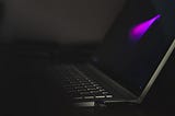 open black laptop against a black background and showing nothing but a fuschia splash of color on the screen