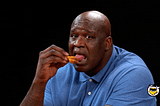 Shaq licking a wing and making a face to indicate that the sauce is hotter than he expected
