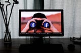 Man looking through binoculars having the Facebook logo on the lenses