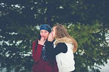 One woman whispering into another woman’s ear.