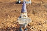 A garden gnome in a barren yard, holding a sign that says “Go away.”