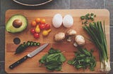 A large cutting board with fresh vegetables and a knife.