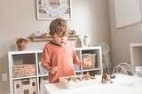 Blond little boy around 3 to 4 years old standing at a white table and playing with a dinosaur