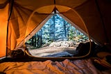 Photo of a forrest seen from within a warm cosy orange tent by Scott Goodwill on Unsplash