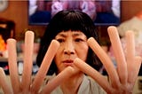 Image from the film Everything Everywhere All at Once where Michelle Yeoh’s hands have become hot dogs
