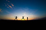 Image of the silhouette of three people on the horizon at sunset, as a metaphor for three roles acting in conjunction. Photo by The Phope on Unsplash