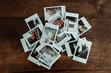 A wooden tabletop with a pile of Instax instant photos.