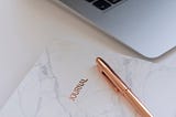 Corner of laptop, pen on journal