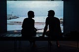 A silhouette of a girl and a boy looking at each other while sitting on an ottoman