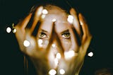 Person holding fairy-lights in front of their face in a way that illuminates only their eyes and hands