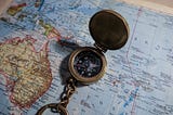 A small pocket compass kept on a coloured map of the world, particularly next to Australia.