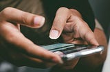 Closeup of 2 hands holding a cell phone with the thumbs poised to test a message