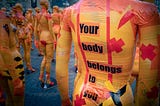 Art installation of several mannequins in red, yellow, and orange tape. The closest one says, “Your body belongs to you.”