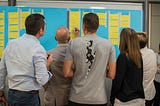People standing around a whiteboard with sticky-notes on it, looking busy