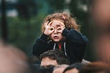 Curly-haired young girl sitting atop a man’s shoulders making round goggles over her eyes with her fingers — image being used by writer to depict looking for life’s purpose