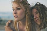 Two young women embracing, looking into their future, one with expectation, one with sadness