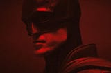 Robert Pattinson as the Batman in the Batman suit basked in red light.