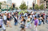 A city street with a lot of people crossing the street, blurred to create a sense of motion and activity