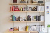 bookshelves arranged with stacks of books, pencil cup full of pens and pencils and some frames