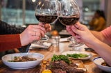 People with wine-glasses at table filled with food.