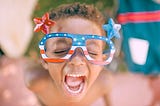 A child in patrotic glasses screaming with their mouth open