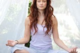 Woman sits with legs crossed, eyes closed, and meditates