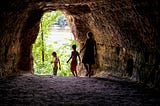 View from behind three boys emerging from a tunnel towards a riverbank in summer.