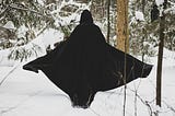 figure walking away in the snow in a black cloak