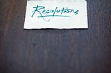 A small rectangular piece of paper with “resolutions” written on it placed on a table.