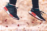 Sneaker-clad feet and lower leg shown jumping up from leaf-strewn ground