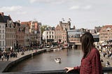 A picture capturing an individual observing a town beside a river bustling with boating activities.