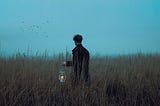 A man in a meadow holding a lantern that is dimly lit