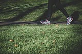 A person walking along a pathway. Only their legs are on view. They are wearing trainers and black leggings. There is grass in the foreground.